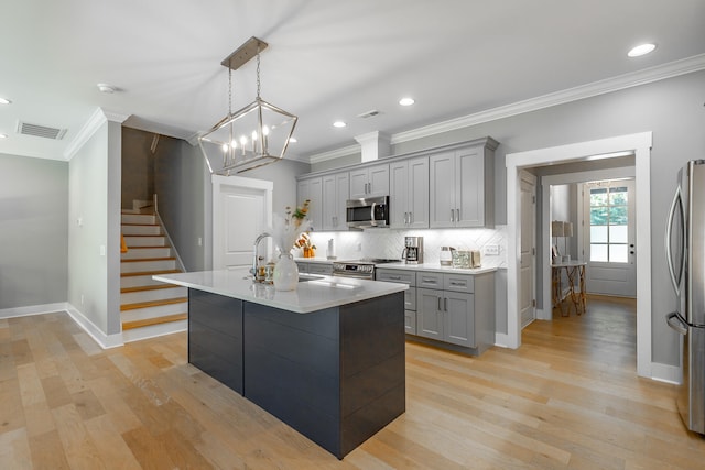 kitchen featuring appliances with stainless steel finishes, pendant lighting, gray cabinets, and an island with sink