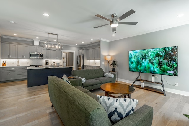 living room with sink, crown molding, ceiling fan with notable chandelier, and light hardwood / wood-style floors