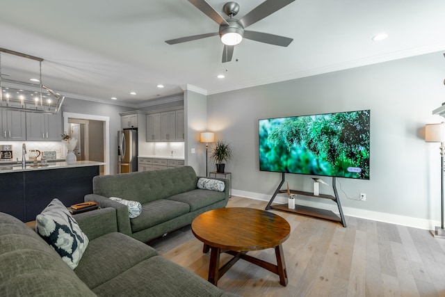 living room with light hardwood / wood-style flooring, ornamental molding, sink, and ceiling fan with notable chandelier