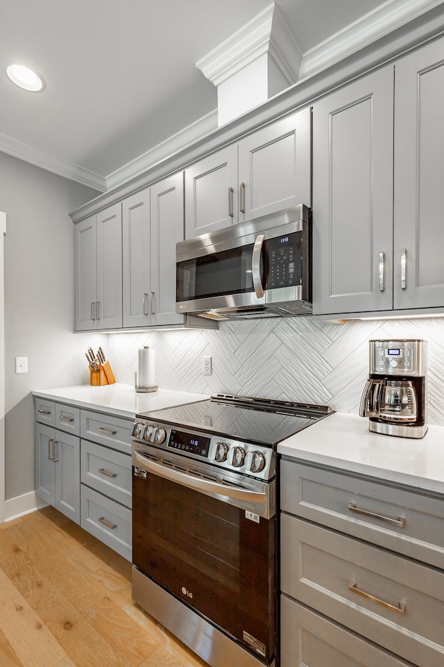 kitchen featuring gray cabinetry, appliances with stainless steel finishes, light hardwood / wood-style floors, crown molding, and decorative backsplash