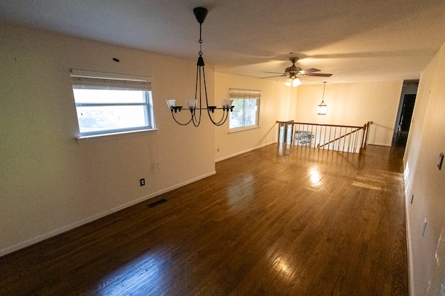 empty room featuring ceiling fan with notable chandelier, a healthy amount of sunlight, and dark hardwood / wood-style floors