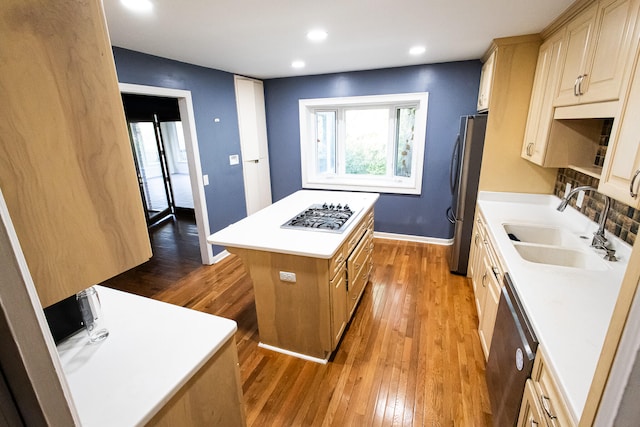 kitchen with light brown cabinetry, stainless steel appliances, sink, wood-type flooring, and a kitchen island