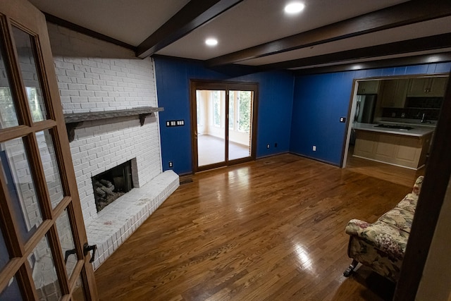 unfurnished living room with dark hardwood / wood-style floors, beam ceiling, and a brick fireplace