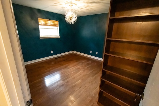 unfurnished room featuring wood-type flooring and an inviting chandelier