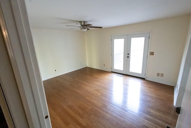 empty room featuring french doors, ceiling fan, and dark wood-type flooring