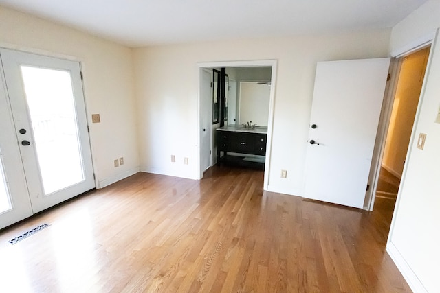 unfurnished bedroom with ensuite bathroom, french doors, sink, and hardwood / wood-style flooring