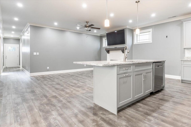 kitchen featuring hardwood / wood-style flooring, hanging light fixtures, a center island with sink, stainless steel dishwasher, and light stone counters