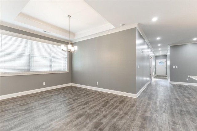 spare room with a raised ceiling, ornamental molding, an inviting chandelier, and dark hardwood / wood-style floors