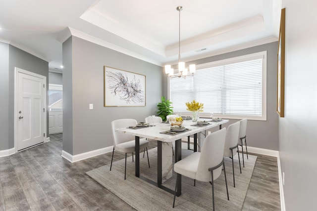 dining area with dark wood-type flooring, a notable chandelier, ornamental molding, and a tray ceiling