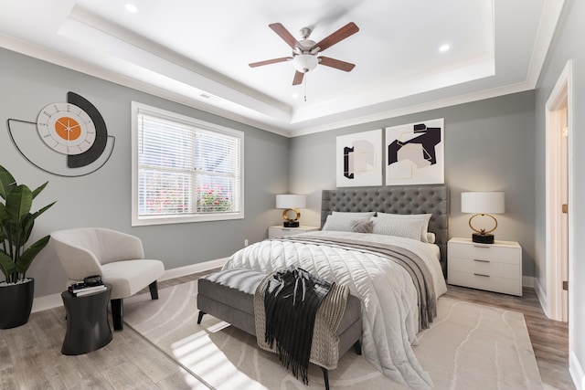 bedroom featuring ornamental molding, ceiling fan, light wood-type flooring, and a raised ceiling