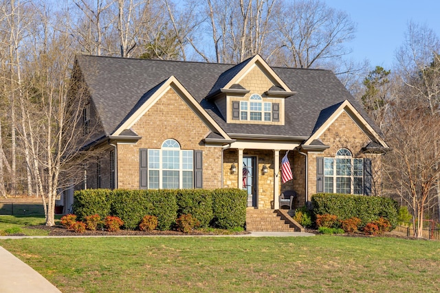 view of front of property featuring brick siding, roof with shingles, and a front yard