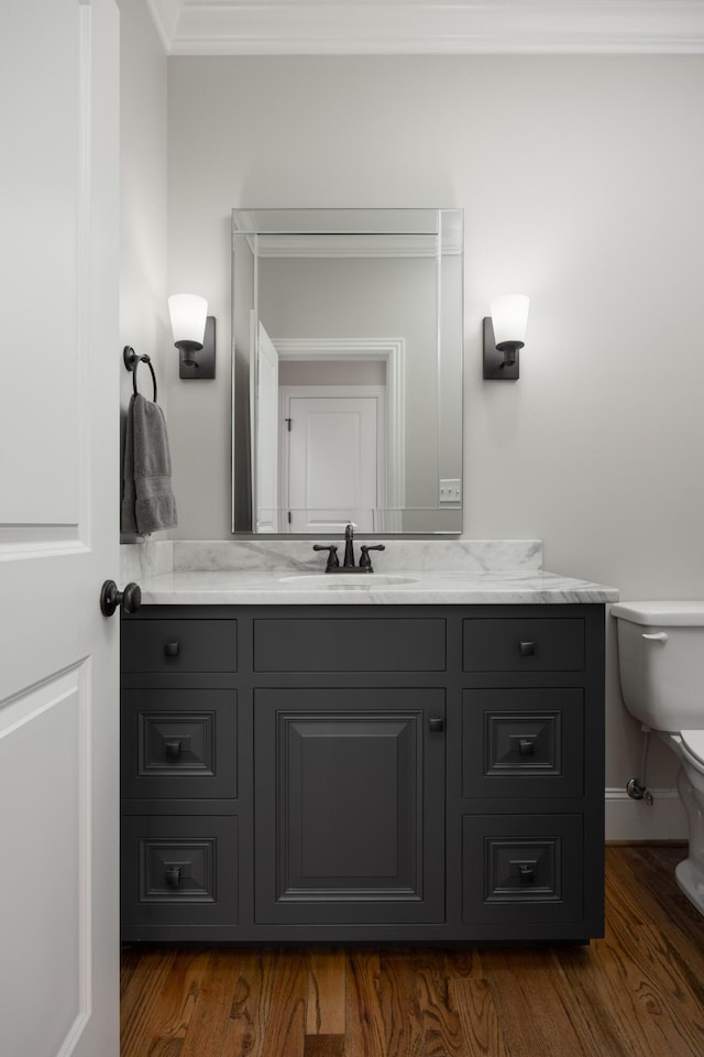 half bath featuring vanity, crown molding, toilet, and wood finished floors