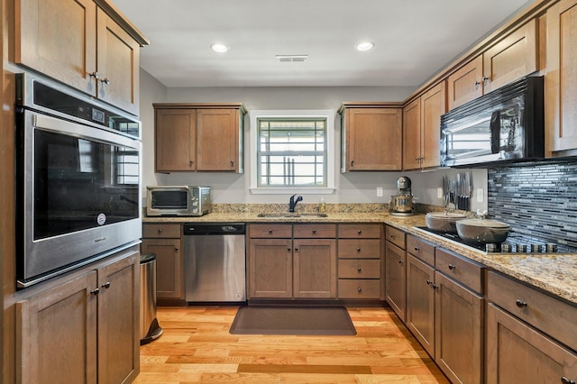 kitchen featuring backsplash, sink, black appliances, light wood-type flooring, and light stone counters