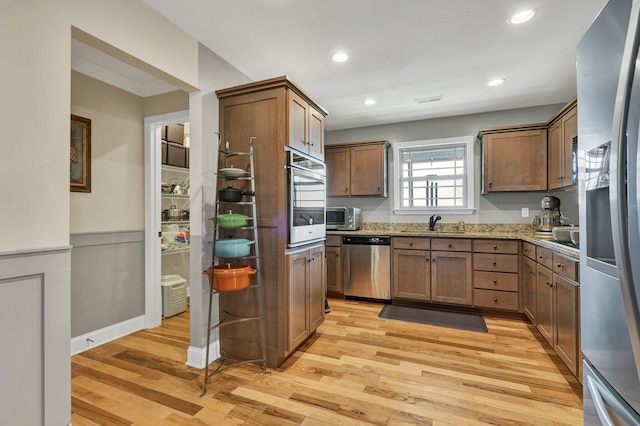 kitchen with appliances with stainless steel finishes, light stone countertops, sink, and light hardwood / wood-style floors