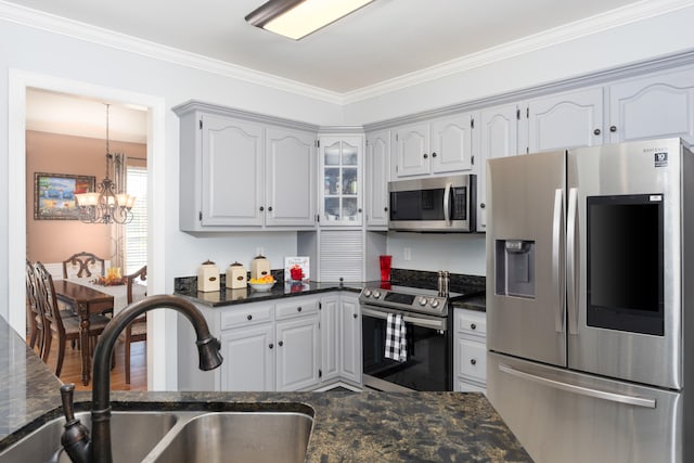 kitchen with dark stone countertops, ornamental molding, sink, an inviting chandelier, and appliances with stainless steel finishes