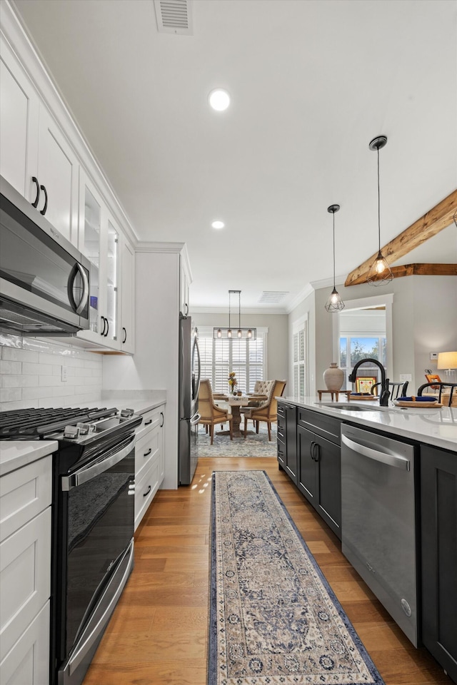 kitchen with tasteful backsplash, hanging light fixtures, stainless steel appliances, light hardwood / wood-style floors, and white cabinets