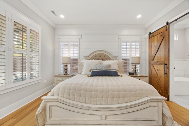 bedroom featuring ornamental molding, a barn door, and light hardwood / wood-style flooring