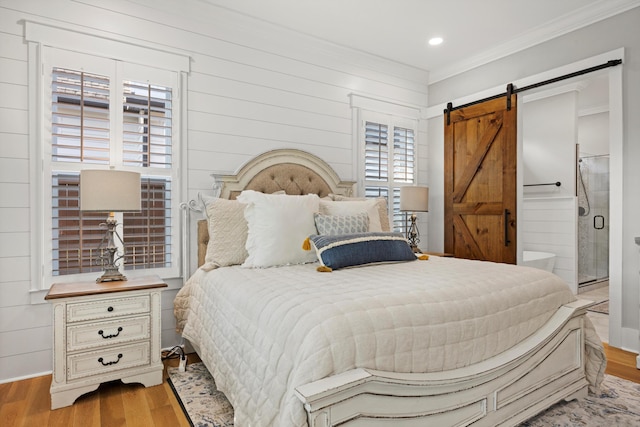 bedroom featuring crown molding, ensuite bathroom, a barn door, and light hardwood / wood-style flooring