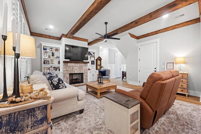 living room featuring beam ceiling, a fireplace, ceiling fan, and light wood-type flooring