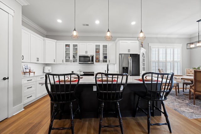 kitchen with decorative light fixtures, stainless steel appliances, white cabinets, and a center island with sink