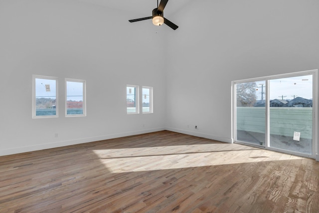 unfurnished living room featuring ceiling fan, a healthy amount of sunlight, light wood-type flooring, and a towering ceiling