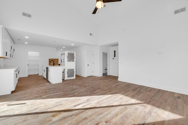 unfurnished living room with light wood-type flooring, a towering ceiling, ceiling fan, and sink