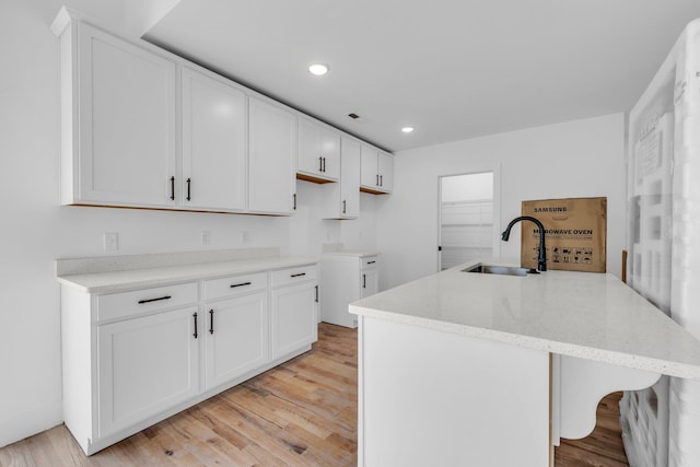 kitchen featuring sink, white cabinets, a kitchen island, and light wood-type flooring