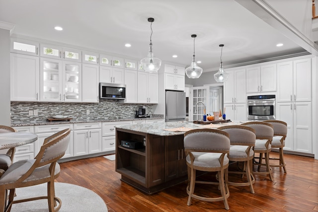 kitchen with stainless steel appliances, a kitchen island with sink, dark wood-type flooring, pendant lighting, and white cabinets