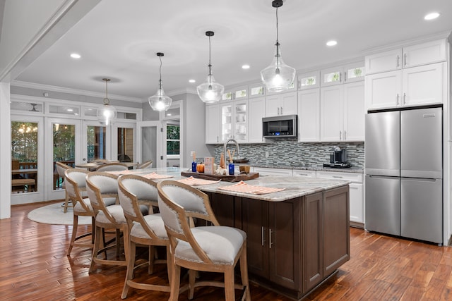 kitchen with white cabinetry, dark wood-type flooring, stainless steel appliances, a kitchen island with sink, and ornamental molding