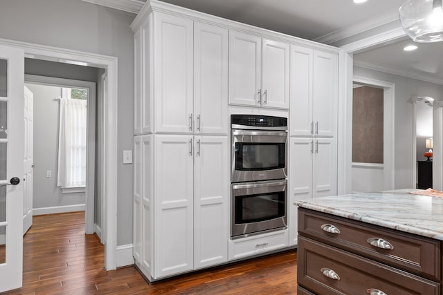 kitchen featuring white cabinets, crown molding, stainless steel double oven, and dark wood-type flooring