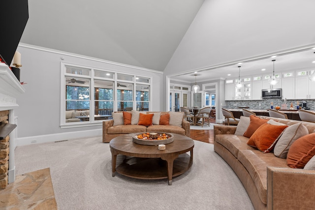 living room featuring light colored carpet, ornamental molding, a fireplace, and high vaulted ceiling