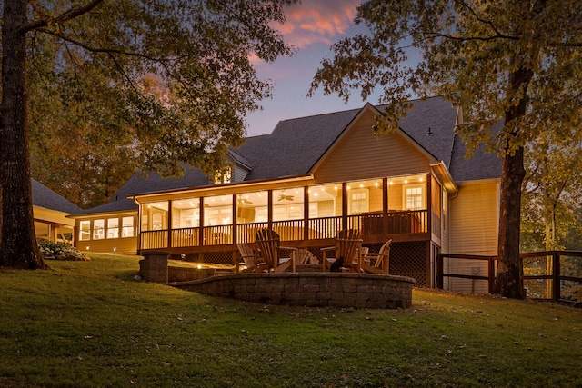 back house at dusk featuring a yard, a deck, and a sunroom