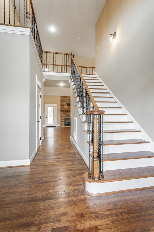 stairs featuring a stone fireplace, a high ceiling, wood finished floors, and baseboards