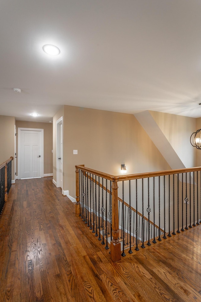 corridor with an inviting chandelier, baseboards, dark wood finished floors, and an upstairs landing