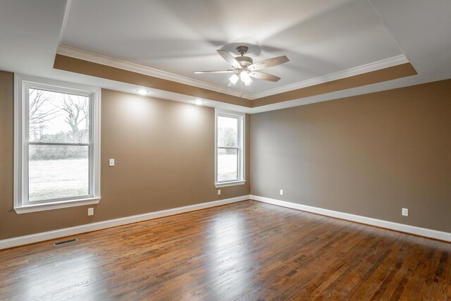 empty room with ornamental molding, a tray ceiling, dark wood finished floors, and visible vents