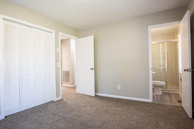 unfurnished bedroom featuring a closet, ensuite bath, and dark colored carpet