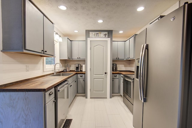 kitchen featuring appliances with stainless steel finishes, butcher block counters, a sink, gray cabinetry, and recessed lighting