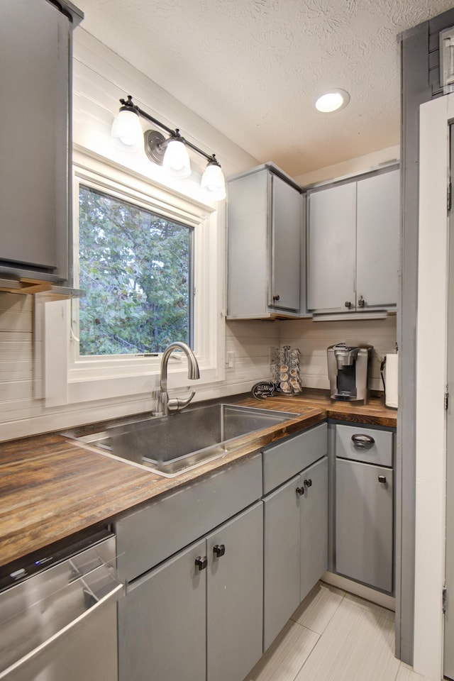 kitchen with butcher block counters, dishwasher, gray cabinetry, a sink, and a textured ceiling