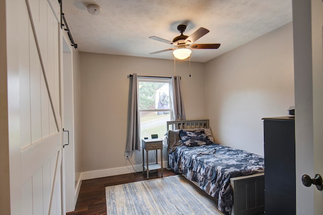 bedroom featuring ceiling fan, dark hardwood / wood-style floors, a textured ceiling, and a barn door