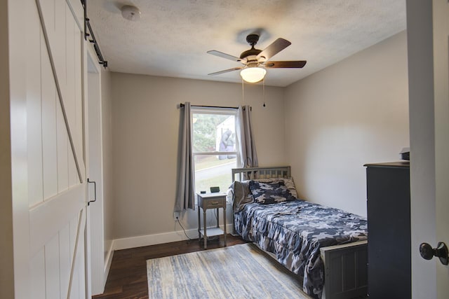 bedroom with baseboards, wood finished floors, a textured ceiling, ceiling fan, and a barn door