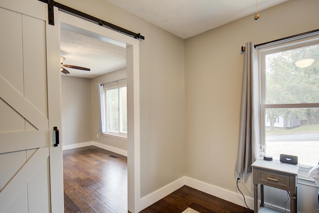 spare room featuring a barn door, dark wood-style floors, baseboards, and a ceiling fan