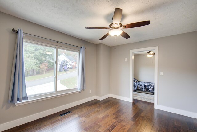 spare room featuring baseboards, dark wood finished floors, ceiling fan, and a textured ceiling