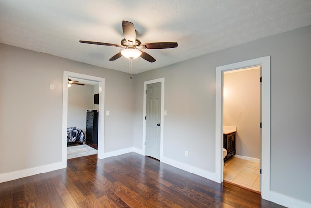 unfurnished bedroom featuring ceiling fan, a textured ceiling, ensuite bathroom, dark wood-type flooring, and a closet