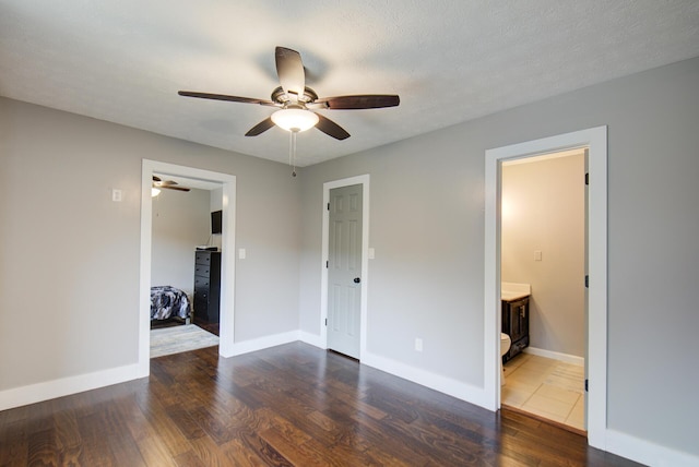 unfurnished bedroom featuring wood finished floors, baseboards, ensuite bath, and a ceiling fan