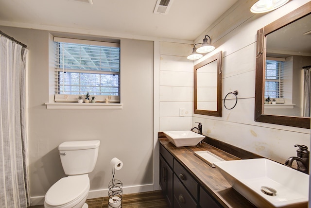 bathroom with toilet, wood finished floors, baseboards, and double vanity