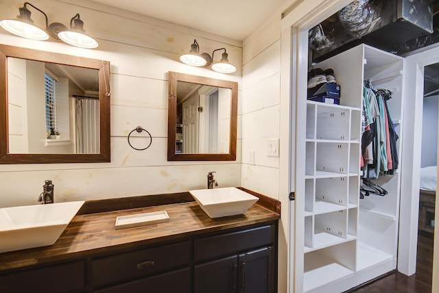 full bathroom featuring a spacious closet, double vanity, and wood finished floors