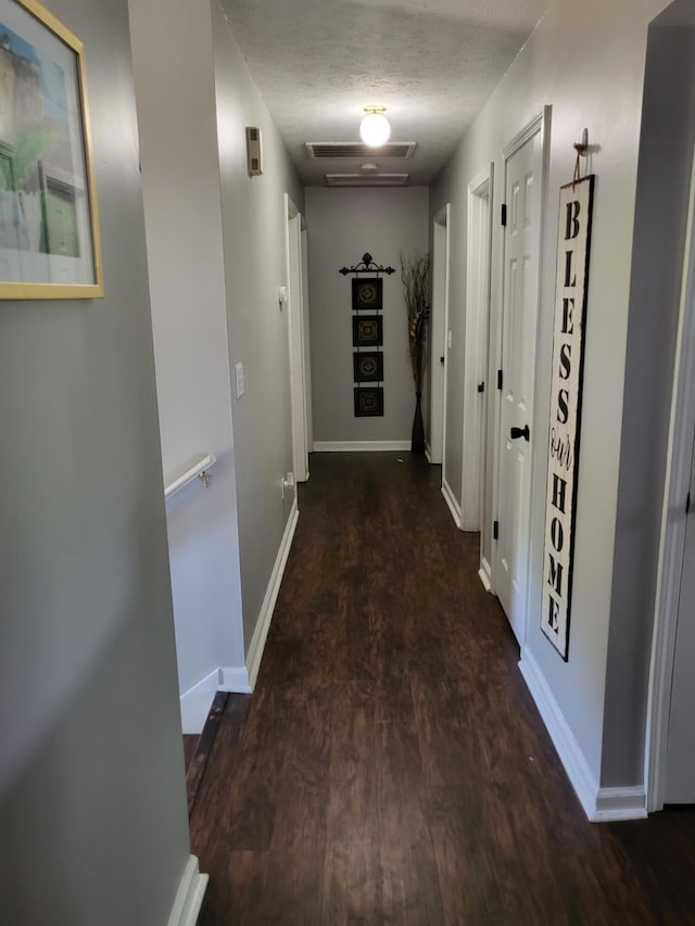 corridor with a textured ceiling and dark hardwood / wood-style flooring