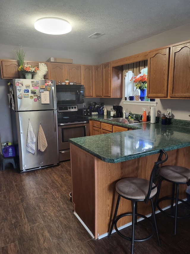 kitchen with sink, a textured ceiling, kitchen peninsula, stainless steel appliances, and dark hardwood / wood-style floors