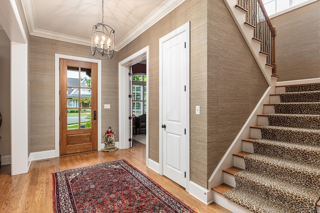 foyer entrance with crown molding, wood-type flooring, and a notable chandelier