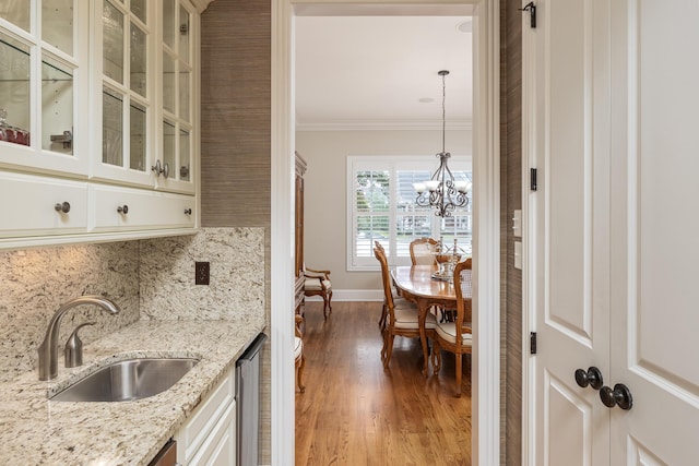 kitchen with pendant lighting, sink, backsplash, ornamental molding, and light stone counters